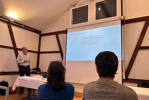 Mann steht vor einer gebeamten Präsentation und erklärt etwas.