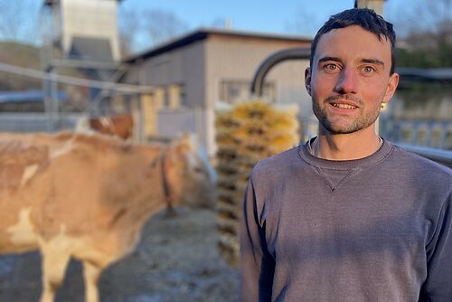 Ein Landwirt mit einer Kuh im Hintergrund.