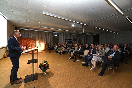 Mann steht an einem Rednerpult vor sitzendem Publikum