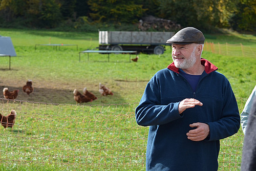 Der Landwirt steht vor einem Geflügel-Auslauf im Freien. 