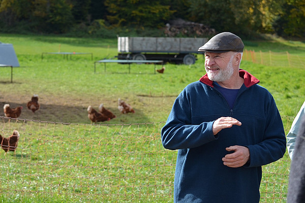 Der Landwirt steht vor einem Geflügel-Auslauf im Freien. 