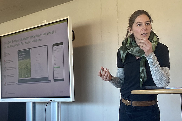 Eine Frau referiert neben einem Bildschirm mit einer Powerpoint-Präsentation. 
