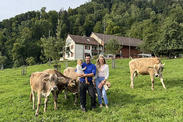 Eine Frau und ein Mann mit Kind posieren mit Rindern auf einer Weide.