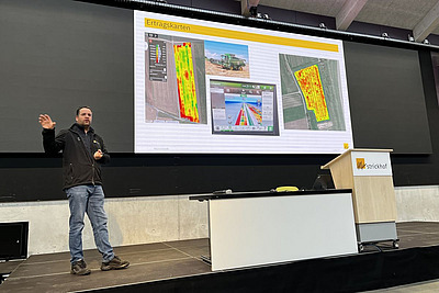 Mann steht vor einer Präsentation auf der Satellitenaufnahmen von Flächen zu sehen sind.