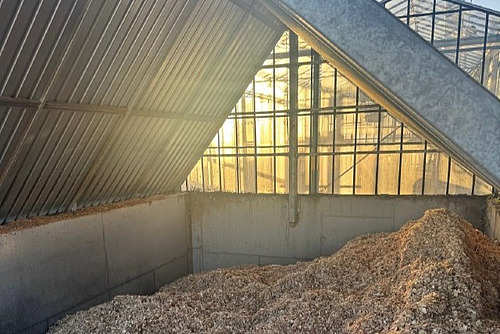 Holzschnitzel vor einem Gewächshaus.