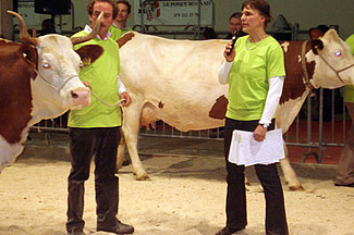 Anet Spengler steht vor einer Kuh , sie spricht ins Mikrofon und gibt ein Kommentar zu dieser Kuh. Hinter der Kuh ist Biolandwirt Andreas Wüthrich zu sehen. Das Bild stammt von einer Viehschau in Lausanne im Januar 2012.
