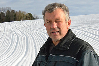 Ein Mann steht vor einem verschneiten Feld und schaut in die Kamera. 