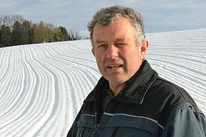 Ein Mann steht vor einem verschneiten Feld und schaut in die Kamera. 