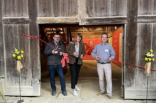 Zwei Männer und eine Frau durchschneiden ein Band zur Eröffnung einer Ausstellung. 