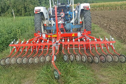 Rote Hackmaschine hinter einem kleinen Traktor.r.