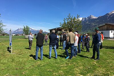 Referent und Personengruppe auf einer Wiese unter blauem Himmel