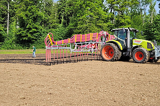 Traktor mit Schleppschlauch bringt Pflanzenkohle mit Gülle auf dem Versuchsfeld aus.