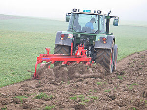 Ein Traktor zieht ein Stoppelhobel auf einer Wiese und bricht die Wiese um