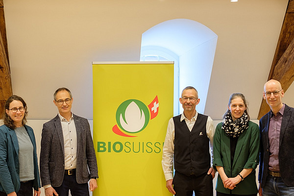 Drei Männer und zwei Frauen stehen neben einem Rollup mit einer Bioknospe. 