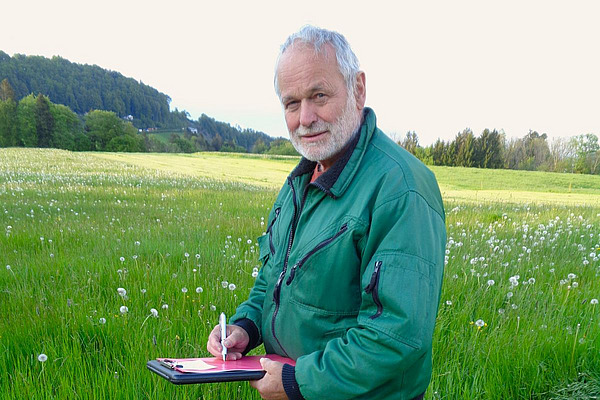 Tobias Brülisauer steht mit einem Klemmbrett auf einer Wiese.