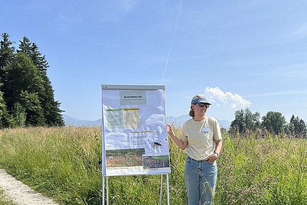Theres Rutz steht in einer Buntbrache und präsentiert auf einer Stellwand die Vor- und Nachteile dieser Biodiversitätsfördermassnahme.