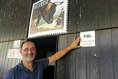 Ein Mann zeigt lächelnd auf ein FiBL-Plakette