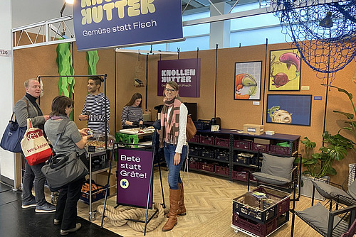 Eine Frau steht in einem Messestand, der reich möbliert ist.