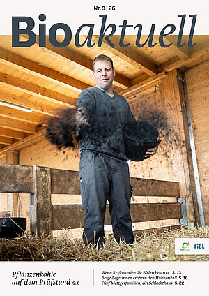 Titelseite Bioaktuell 3|26: Ein Mann streut Pflanzenkohle auf Heu.