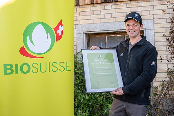Ein Mann mit Baseballcap steht neben einem Rollup und hält ein Diplom in der Hand. 