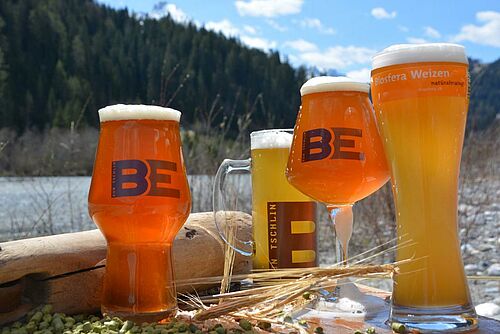 vier volle Biergläser vor See und Wald im Hintergrund