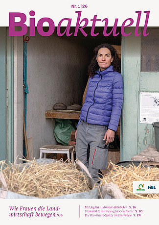 Titelseite Bioaktuell 01|26: Eine Frau steht angelehnt an einem Türrahmen, im Vordergrund stehen zwei Säcke mit Heu.