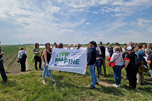 Menschen stehen auf einem Feld und halten eine Fahne mit dem Aufdruck "OH-FINE".