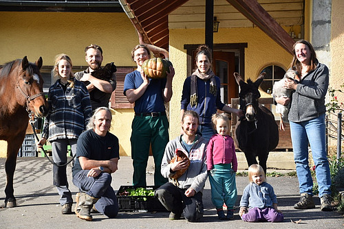Eine Gruppe von Menschen verschiedenen Alters posieren mit einem Pferd, einem Esel, einem Huhn, einer Gans und einer Katze. 