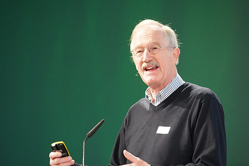 Ein Mann referiert vor einer grünen Wand.