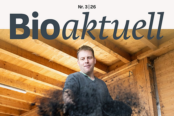 Titelseite Bioaktuell 3|26: Ein Mann streut Pflanzenkohle auf Heu.