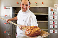 Bäcker nimmt mit Holzschaufel ein Brot aus dem Ofen