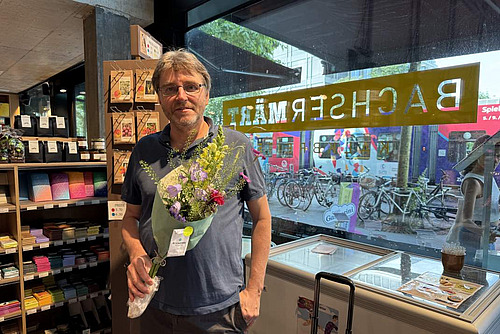 Ein Mann steht mit einem Blumenstrauss in einem Laden.