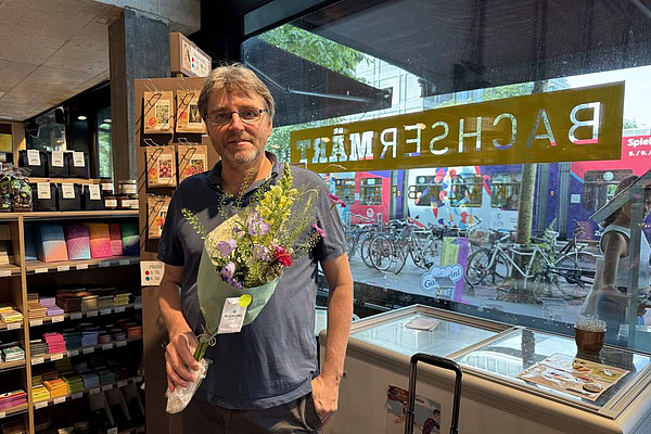 Ein Mann steht mit einem Blumenstrauss in einem Laden.