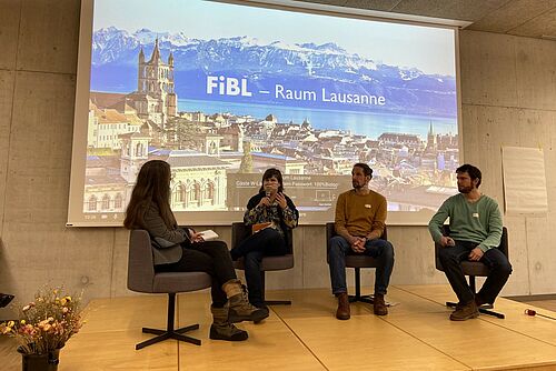 Eine Podiumsrunde vor einer Leinwand.