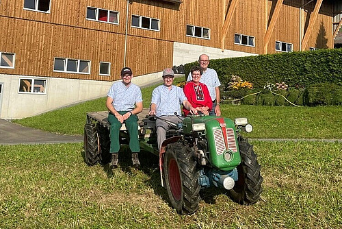 Eine Frau und drei Männer posieren auf und neben einem grünen Einachser vor einem Stallgebäude.
