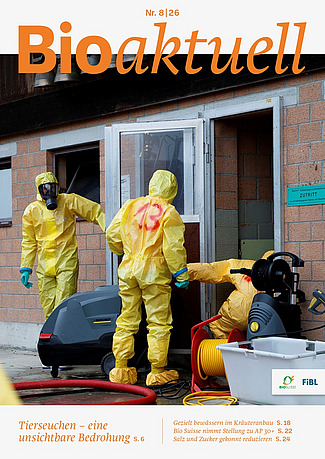 Titelseite Bioaktuell 8|26: Drei Menschen in Schutzanzügen und Atemmasken beim Eingang zu einem Stall.