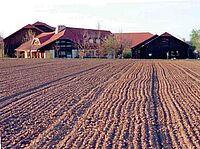 Hintergrund: Bauernhof. Vordergrund frisch angesäter Acker