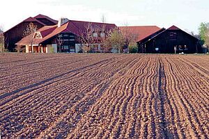 Hintergrund: Bauernhof. Vordergrund frisch angesäter Acker