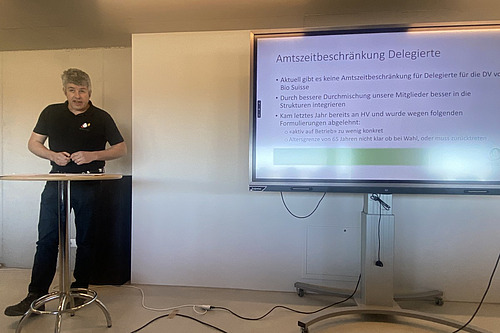 Ein Mann steht neben einem Bildschirm mit einer Powerpoint-Präsentation. 