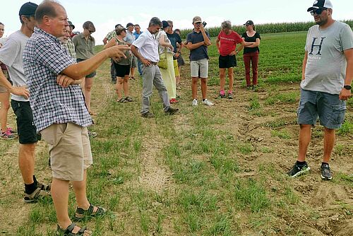 Mehrere Personen stehen auf einem Feld, ein Mann erklärt etwas im Vordergrund