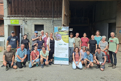 Eine Gruppe von Menschen mittleren Alters steht geordnet beieinander. In ihrer Mitte befindet sich ein Banner des FarmBioNet-Projekts.