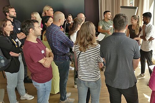 Eine Gruppe von jüngeren Personen diskutiert vor einem Flipchart.