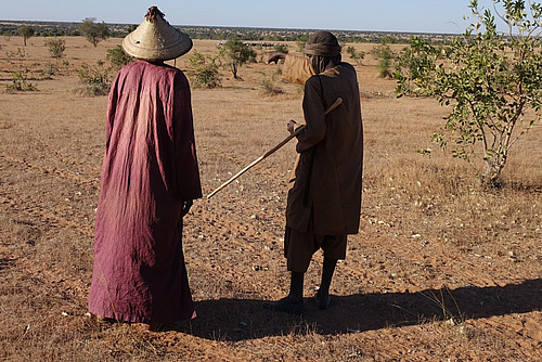 Zwei schwarze Männer diskutieren in einer ariden Umgebung.