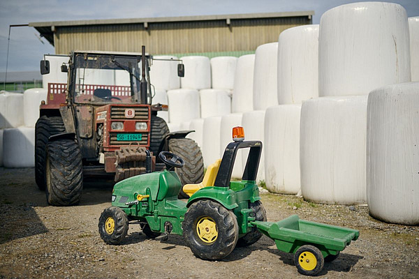 Richtiger Traktor und Spielzeugtraktor von gestapelten weissen Siloballen.