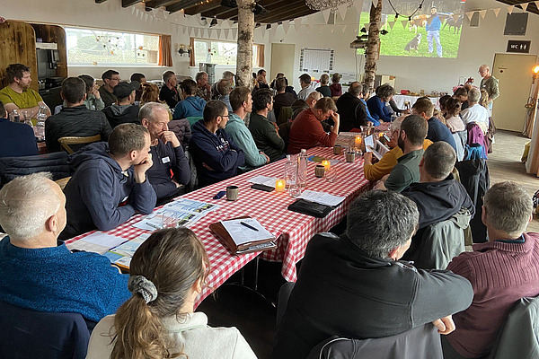 Ein Saal voller Menschen an Tischen mit rotweissen Tischtüchern. 
