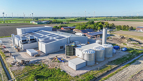 Ein neues Gewerbegebäude umgeben von landwirtschaftlich genutzten Flächen. 