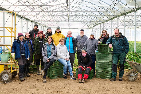 Ein Gruppenbild mit Menschen verschiedenen Alters in einem Treibhaus. 