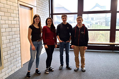 Vier Lernende stehen im Gang eines Schulhauses.