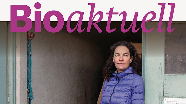 Titelseite Bioaktuell 1|26: Eine Frau steht angelehnt an einem Türrahmen, im Vordergrund stehen zwei Säcke mit Heu.