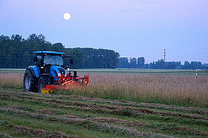 Taktor mit Frontmähwerk beim Mähen einer blühenden Wiese am Abend